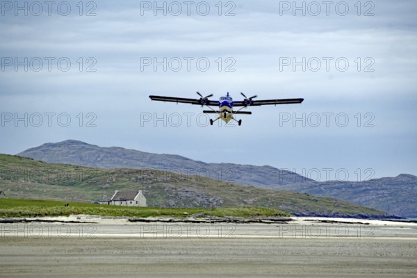 Low flying aeroplane over a runway in mountain landscape with cloudy sky, Isle of Barra, Hebrides,