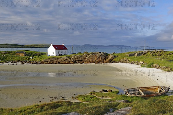 Boat wreck on a sandy beach with a white house and rocks in the background, Isle of Barra,