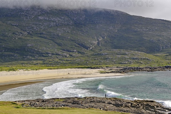 Expansive coastline with beach and waves against a mountain backdrop under a cloudy sky, Castlebay,