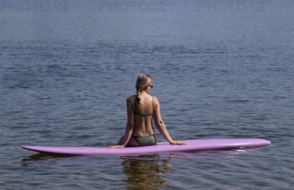 Woman, blonde, in bikini, sitting on board, surfboard, surfboard, purple, back, from behind,