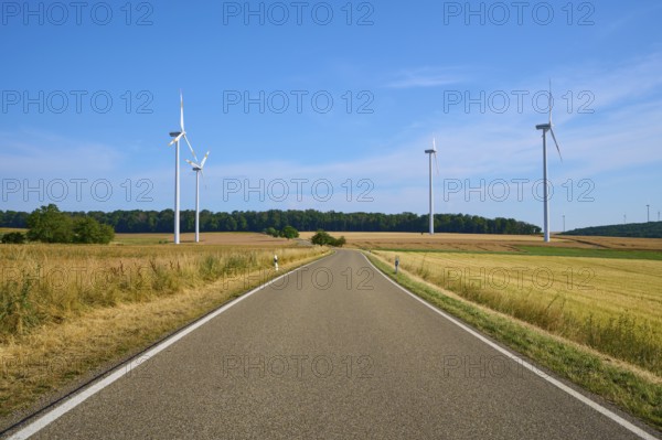 A road leads through fields, flanked by several wind turbines under a clear sky, summer, Wenkheim,