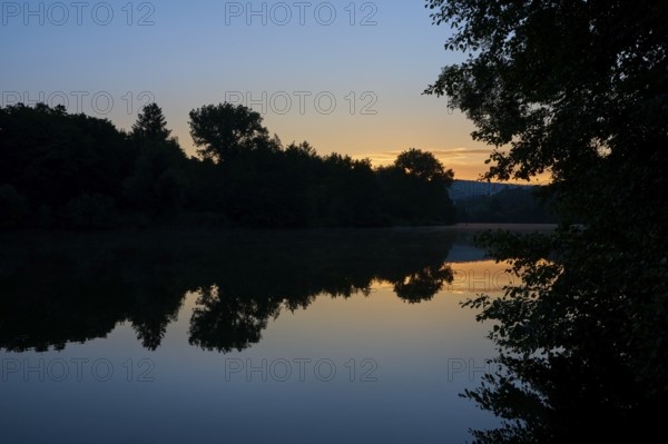 Morning sky over a quiet river Main with trees silhouetted against the orange light, summer,