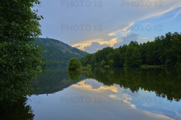 The calm river Main reflects trees and an impressive sky streaked with evening clouds, summer,