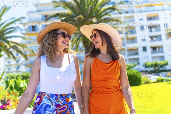 Two female tourists wearing sunglasses and sun hats walk and talk together while enjoying their
