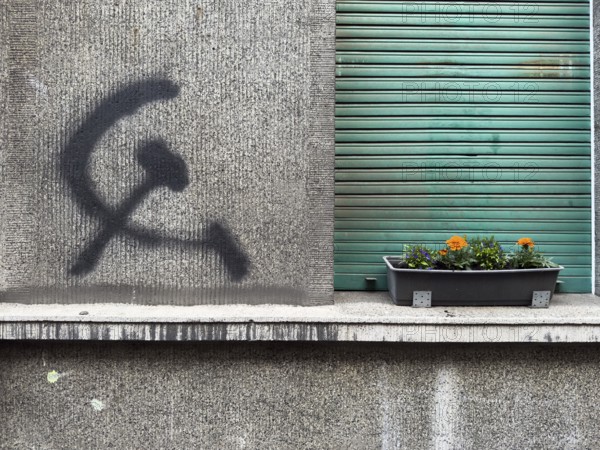A hammer and sickle graffiti on a house wall next to a planted flower box in front of a roller