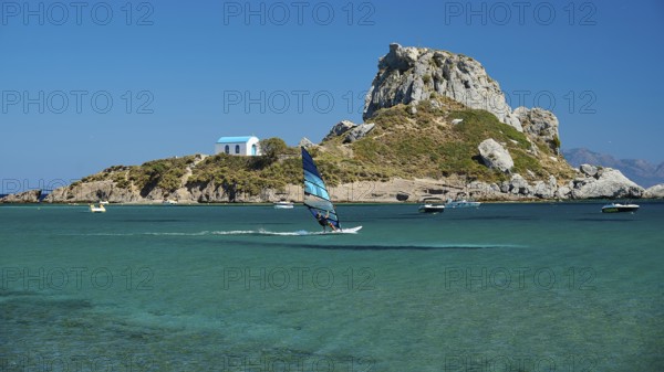 View of island with windsurfer and chapel in bright sunshine, Agios Stefanos Beach, Agios Stefanos