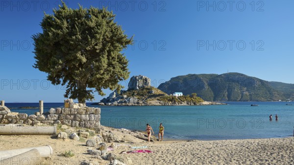 Family on the beach overlooking a green island and clear blue waters, Agios Stefanos Beach, Agios