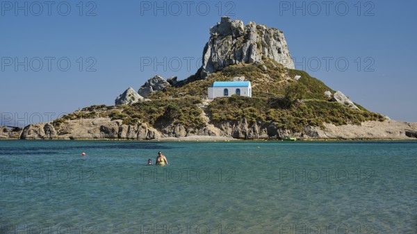 Small chapel with blue roof on rocky island in clear sea, Agios Stefanos Beach, Agios Stefanos
