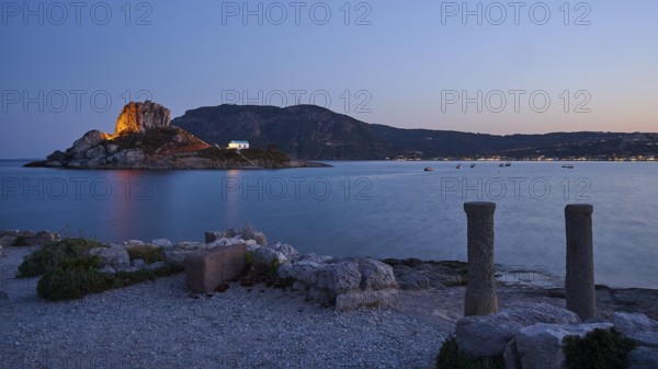 Night view of an island with illuminated rock and a small chapel in the calm water, Agios Stefanos