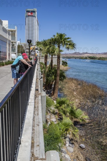 Couple looking at cell phone on sidewalk overlooking jet ski activity on the Colorado River in