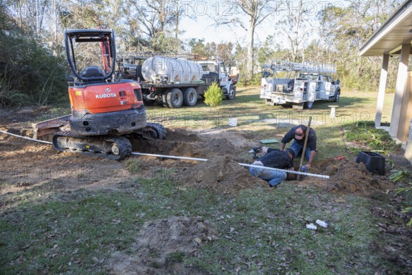 Workers installing pipe connecting new water well to house plumbing in rural area of Gulfport,