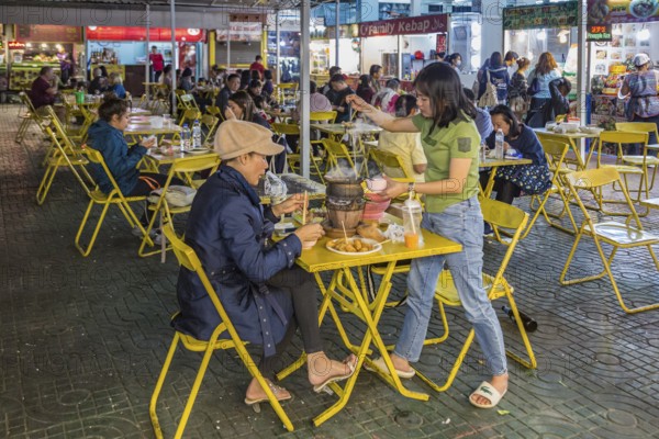 Thai mother and daughter preparing a meal in a hot pot at their table at the night market in