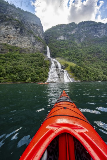 Kayak trip on the Geirangerfjord at the Freier waterfall, tip of a red kayak in the fjord,