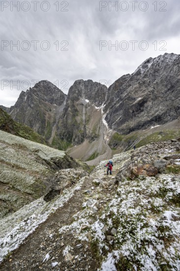 Mountaineer on hiking trail in steep rocky mountain landscape with fresh snow in summer, behind