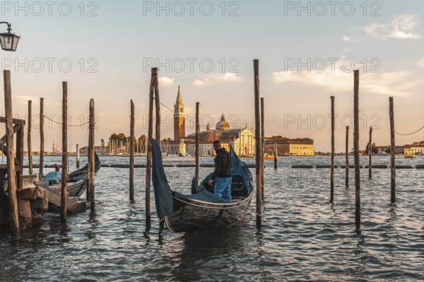 Gondolier preparing his gondola in venice, italy, at sunset, with the church of san giorgio