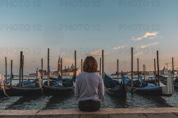 Young woman enjoying the sunset over the venetian lagoon with gondolas moored in the foreground and