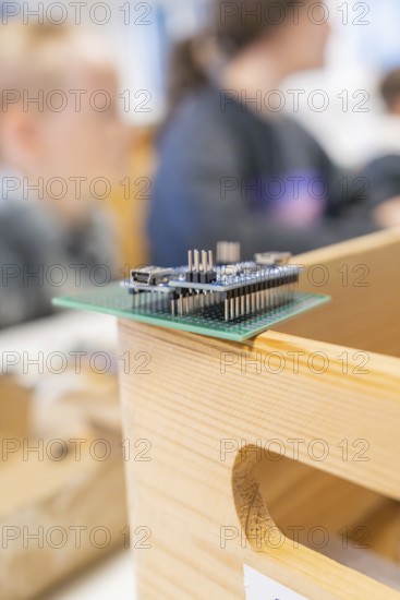 Technological circuit board on a wooden box with blurred people in the background, Nagold Youth