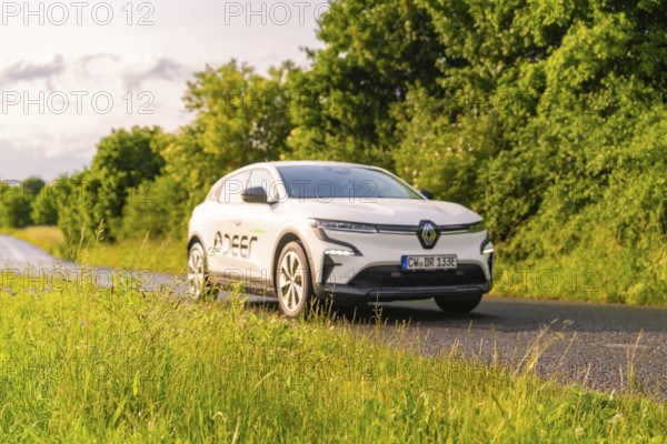 Renault car drives along a green, tree-lined country road, Renault Megane, Deer E Carsharing,