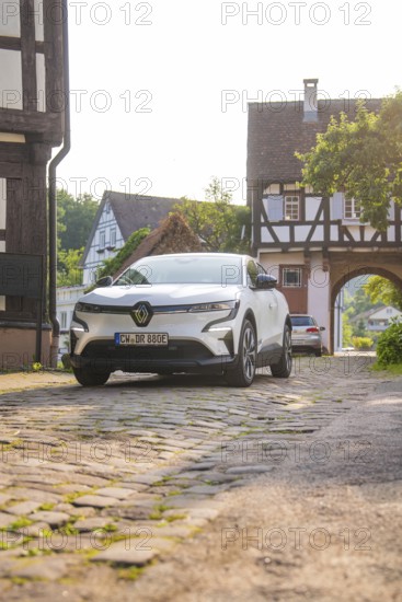 A white car on a cobbled street in a village with half-timbered houses and a summery atmosphere,