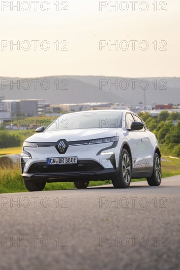Car driving along a road with a view of modern buildings in the background, Renault Megane, Deer E-