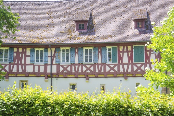 Historic half-timbered house with small windows behind green hedges, event and wedding location
