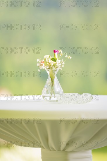 White table with a small flower vase and an ashtray in front of a blurred background, event and