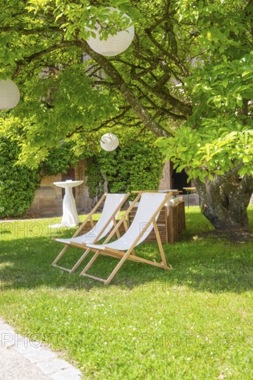 Two deckchairs in the shade of a tree on a green meadow, ideal for relaxation, event and wedding