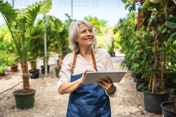 Smiling gardener working in a greenhouse, using a digital tablet while surrounded by vibrant plants
