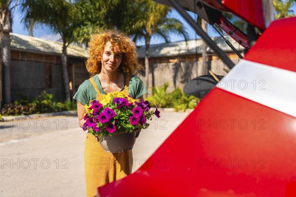 Young gardener carrying colorful petunia flowers to her car trunk after shopping at garden center