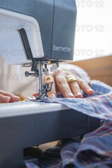 Focus on a sewing machine processing fabric, hand-guided and adorned with a gold ring