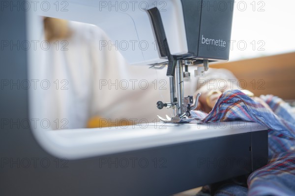 Details of the sewing process with needle and fabric in a well-lit environment, focus on the