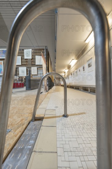 Railing in a gallery corridor with tiled floor and illuminated walls, historical art exhibition in
