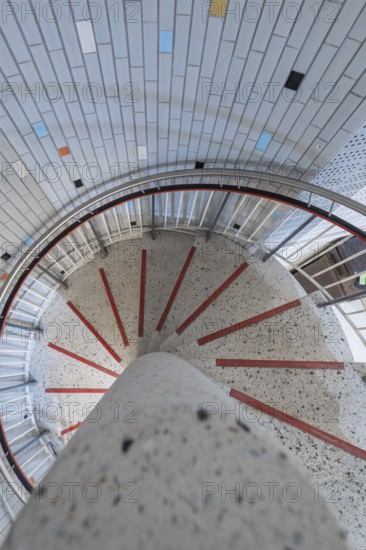 A spiral staircase with colourful tiles and a central concrete pillar, modern architectural design,