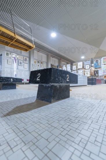 A dark winner's podium stands in an exhibition hall, surrounded by works of art and industrial