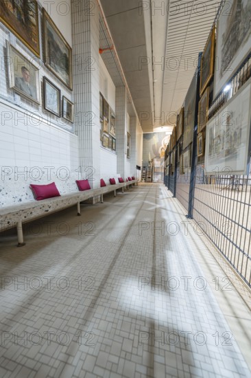 A long corridor in an art gallery with numerous paintings on the walls and a white bench with red