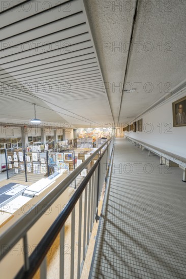 A corridor on the upper floor with a view of a large art gallery decorated with various works,