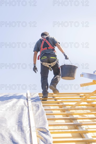 Construction worker with safety belt carrying a bucket on a roof, roof renovation, house