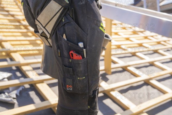 Construction worker on roof construction with tools in his trouser pocket, roof renovation, house