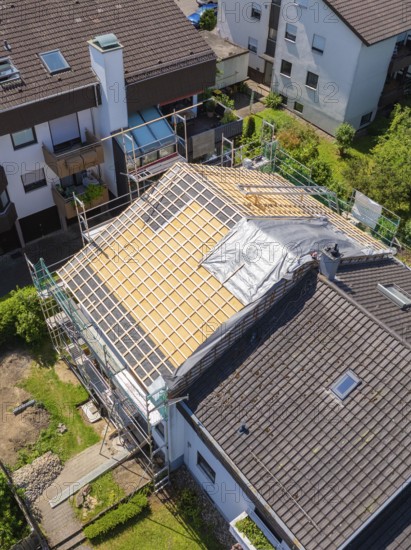 House with scaffolding and part of the roof covered, in a sunny residential area, roof renovation,