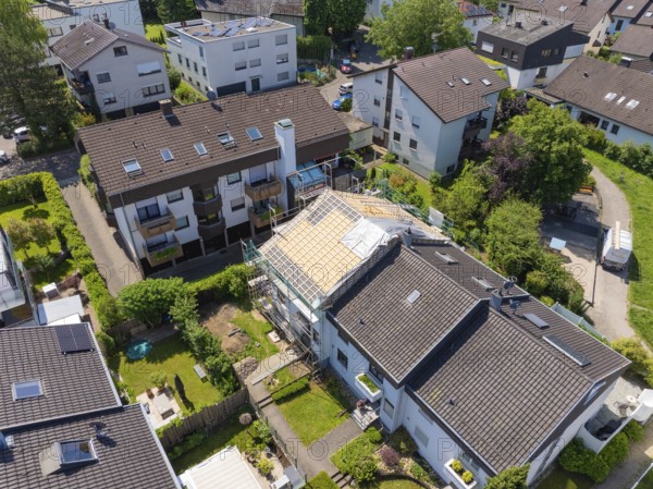 Aerial view of a residential area with a house showing roof work in the middle of green areas, roof