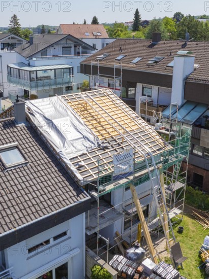 A roof is being renovated or newly built, scaffolding visible, sunny neighbourhood, roof