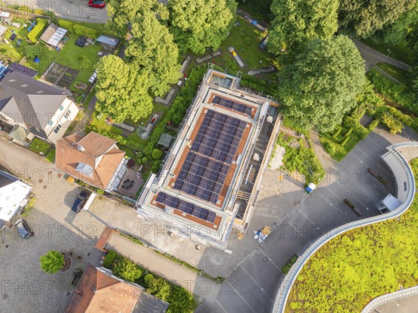 Aerial view of a construction site with solar modules on the roof, surrounded by gardens and