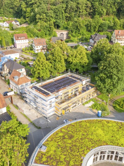 Aerial view of a construction site in a residential area surrounded by trees and green roofs on a