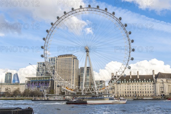 The london eye majestically stands tall on the banks of the river thames, with a boat sailing by