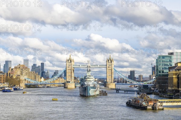 Hms belfast, a town class light cruiser, sailing on the river thames with tower bridge and cloudy