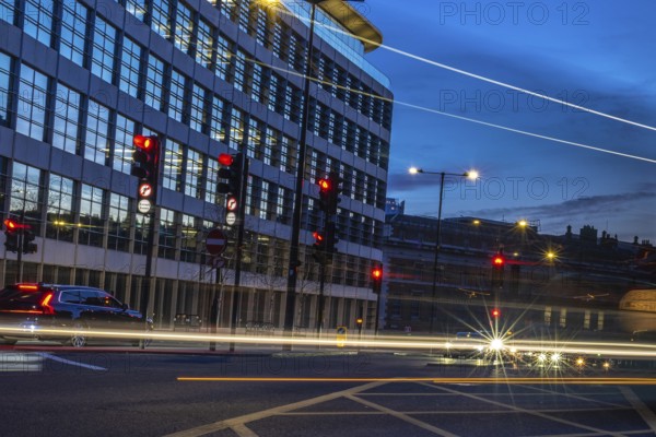 Cars passing by on a london street at dusk, with traffic lights turning red and offices in the