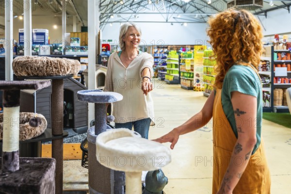 Senior woman buying a cat tree in a pet shop, helped by a young sales assistant, choosing the right