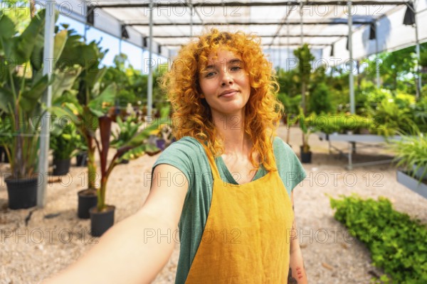 Confident red haired female gardener taking a selfie in a greenhouse, showcasing her passion for