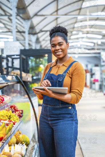 Young supermarket employee managing fresh fruit section inventory using a digital tablet, ensuring