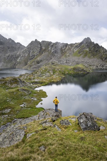 Mountaineer on a rock in front of mountain lakes Wangenitzsee and Kreuzsee, cloudy mountain peaks